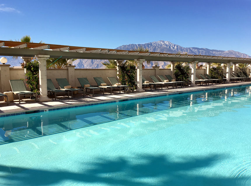 Blue swimming pool with sunloungers and blue sky behind in california desert
