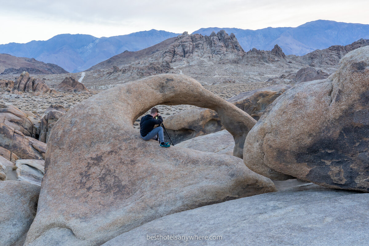 Man with camera on tripod sat on a rock formation taking photos of other rocks at dawn