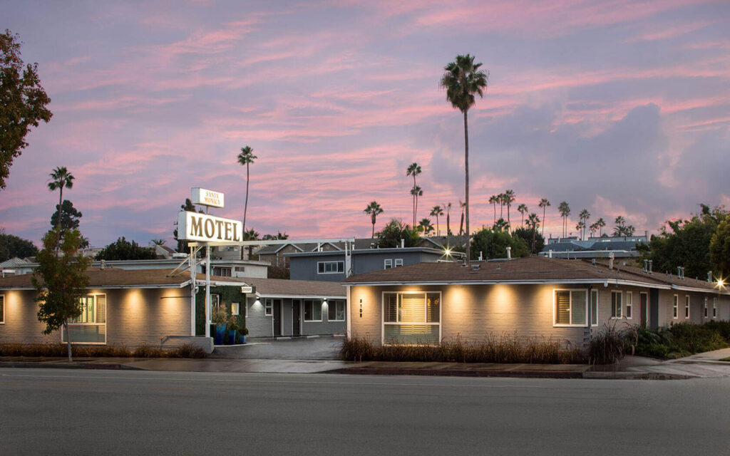 Exterior photo of Santa Monica Motel from afar with whole building in view at dusk pink clouds and lights in motel