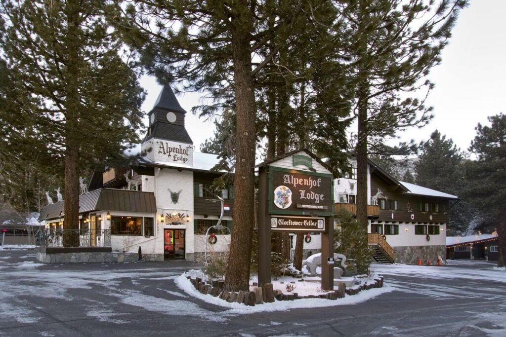Austrian looking building surrounded by trees hotel in Mammoth Lakes CA with light snow on the ground and grey clouds