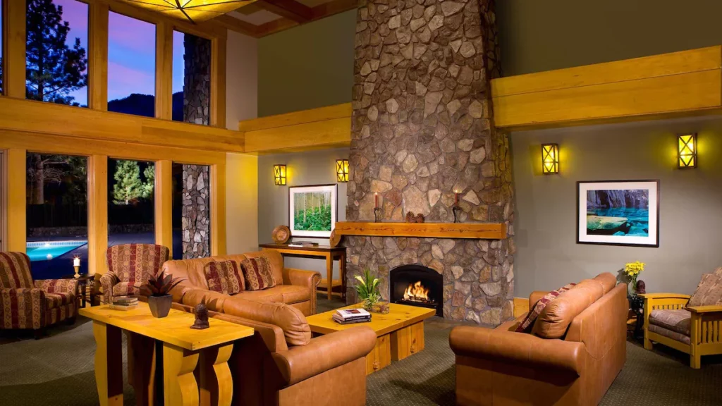 Fireplace and stone chimney with sofas and large glass windows at a hotel in Mammoth Lakes