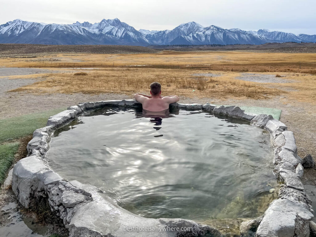 Man bathing in a natural hot spring in Northern California near Mammoth Lakes with Sierra Nevada mountains in distance
