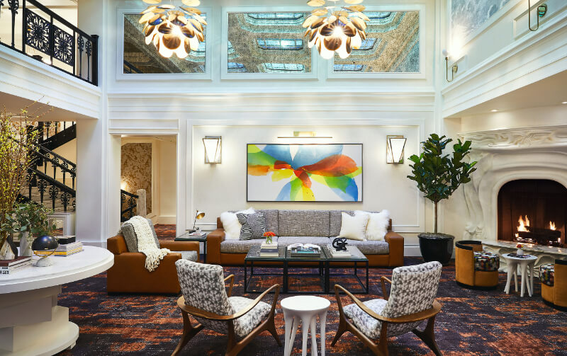 Lobby of a hotel in San Francisco with tables and chairs on a carpet high ceiling 2 story room with paintings