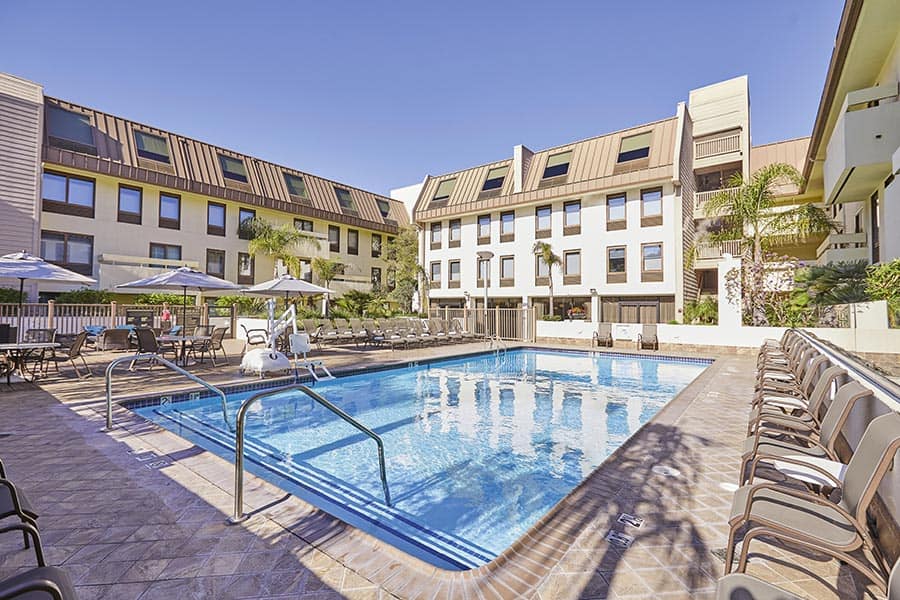 Outdoor swimming pool with chairs and L shaped building Riu Plaza Hotel in San Francisco on a bright day
