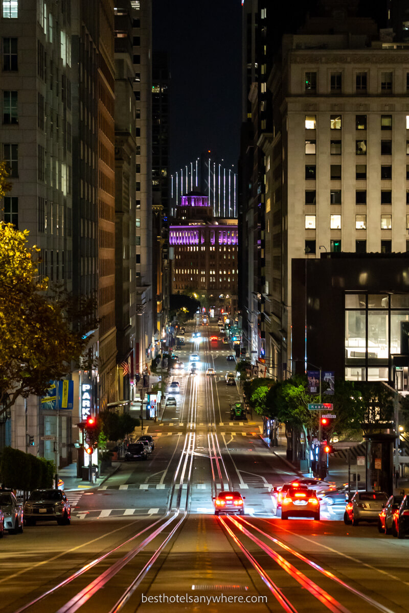 Typical San Francisco street with tram lines running through buildings to the Oakland Bridge at night
