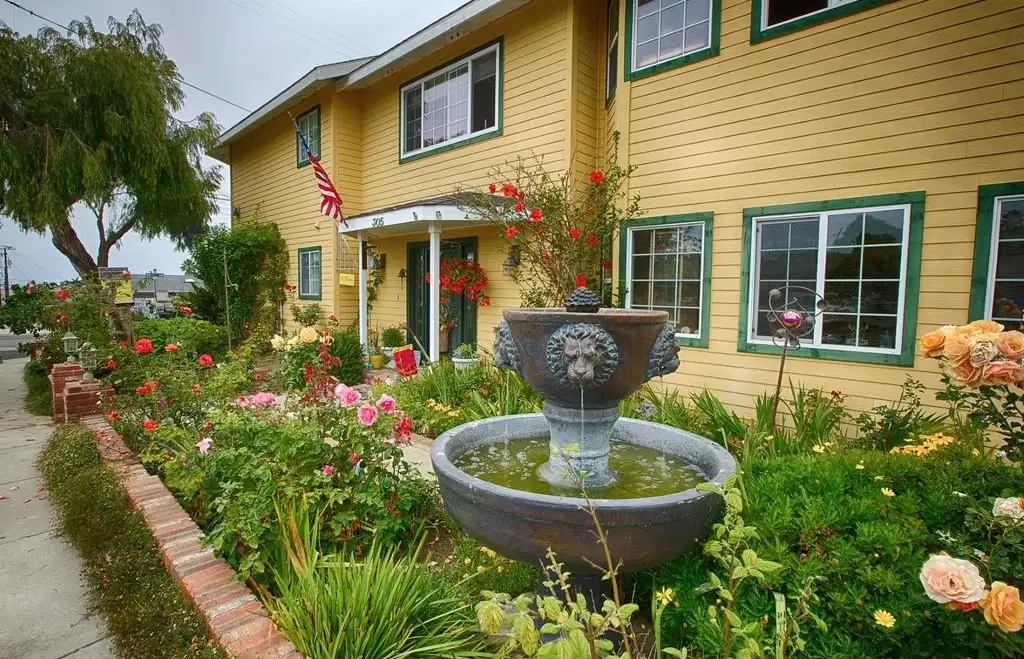 Exterior photo of yellow building and colorful garden with stone bird bath marina street inn one of the best cheap hotels in Morro Bay CA