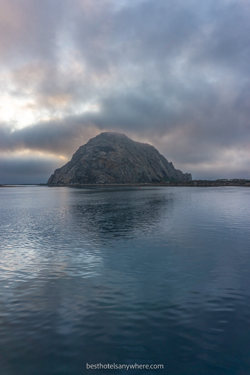 Morro Rock at sunset with thick clouds lighting up beyond blue ocean water