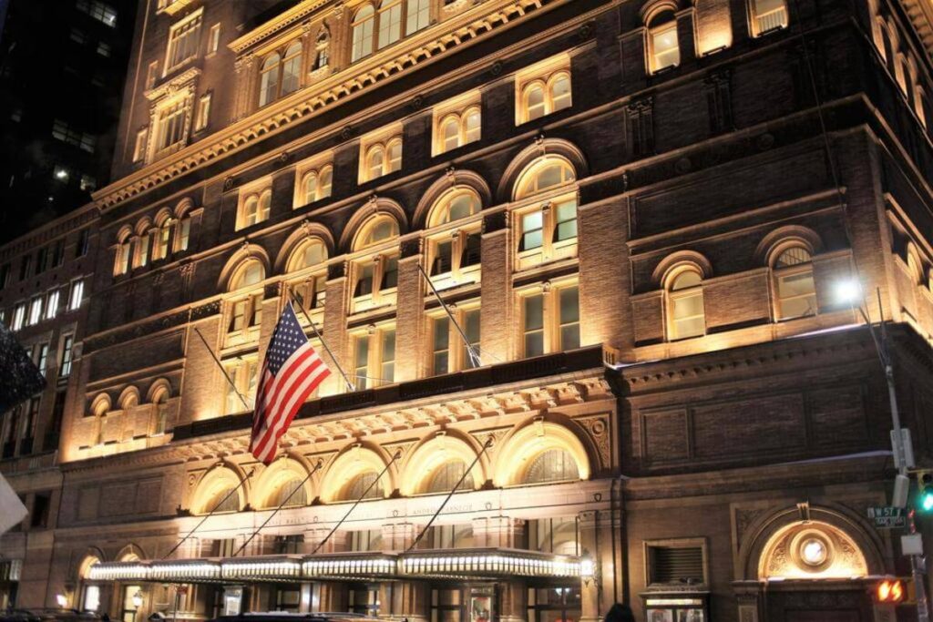 Exterior photo of the Carnegie boutique hotel near Central Park lit up at night with American flag flying