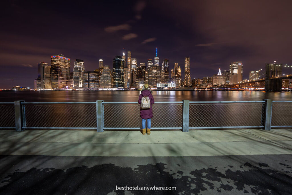Person looking at Downtown Manhattan skyline from Brooklyn Bridge Park at night