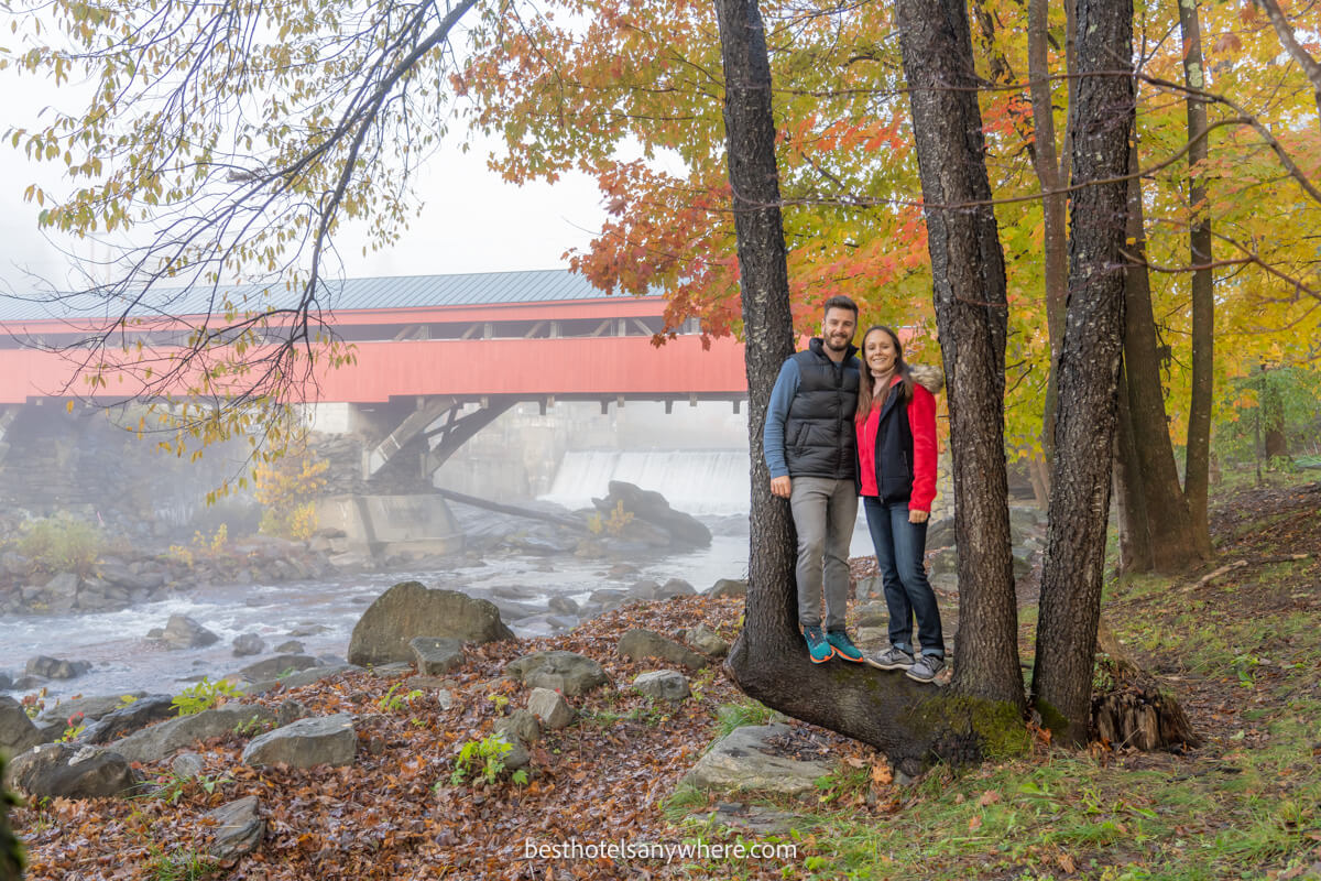 Mark and Kristen Morgan from Best Hotels Anywhere stood in a natural tree frame on the riverbank next to Taftsville Covered Bridge near Woodstock in Vermont