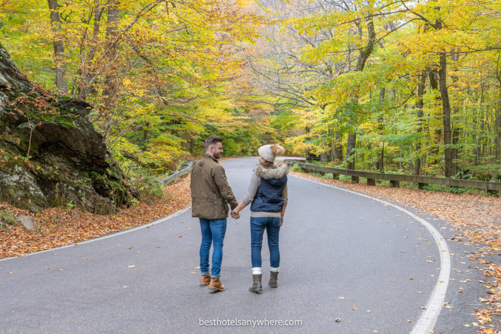 Mark and Kristen Morgan from Best Hotels Anywhere walking down a narrow winding road in Stowe VT with fall foliage colors in the trees