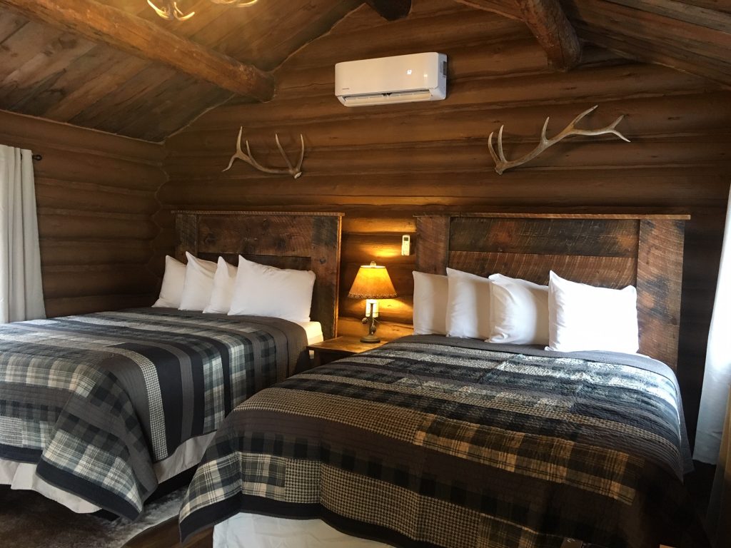 Inside a guest bedroom at a West Yellowstone hotel with two beds and elk horns backed by wooden logs