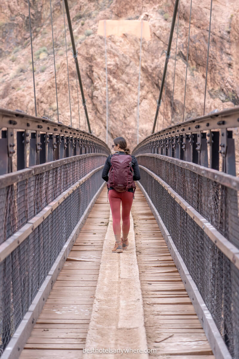 Hiker crossing a long and narrow suspension bridge on a wooden path