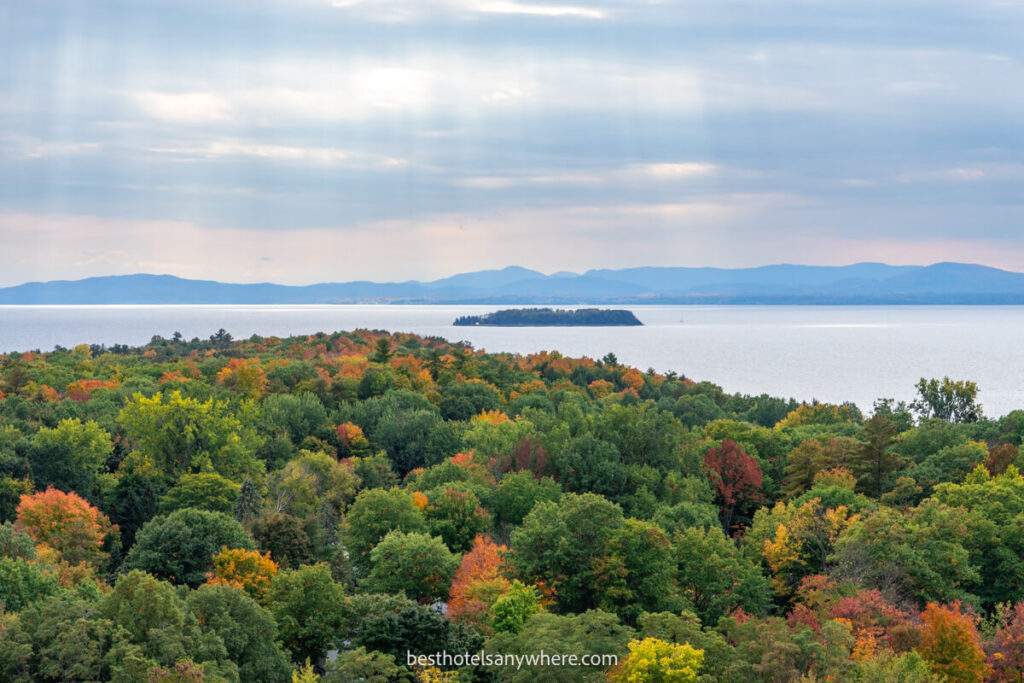 Sun beams bursting through clouds onto Lake Champlain and hundreds of trees with green leaves and some fall foliage colors