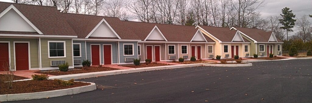 Row of motel style lodges with different colored facades next to a parking lot