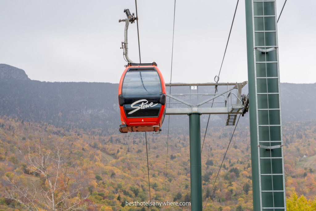 Red and black gondola ski lift on a cloudy day with autumnal colored leaves in the background