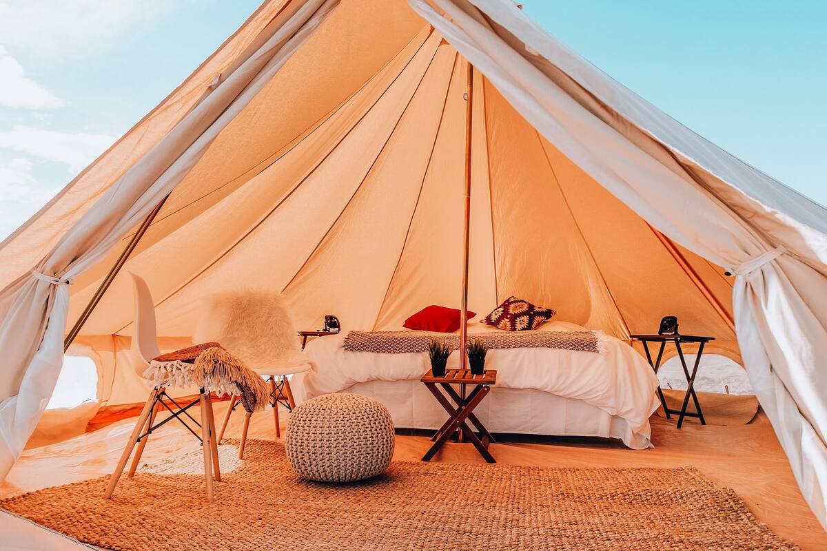 Inside a glamping tent with bed, chair and table on a sunny day
