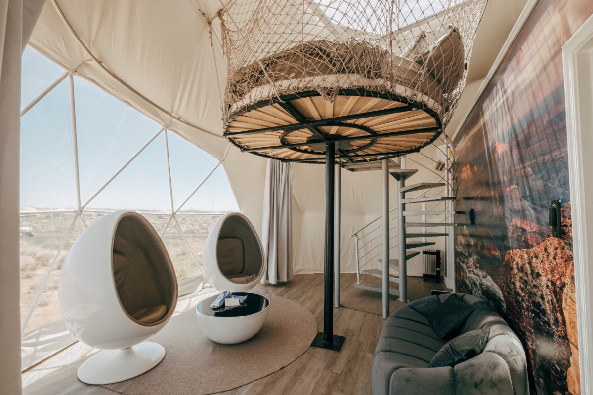 Inside a luxury glamping tent with two egg shaped chairs and a spiral staircase leading up into the tent