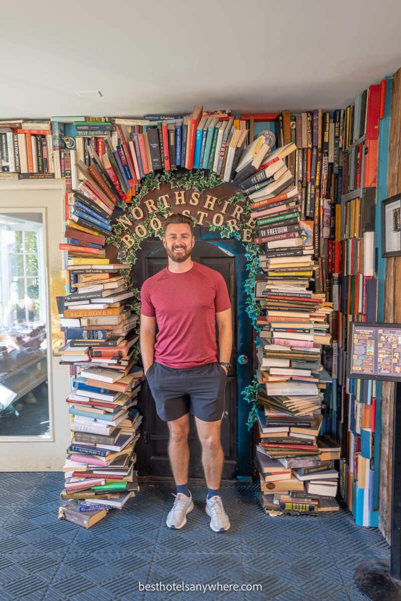 Tourist in shorts and t-shirts stood underneath an arch made of books inside a bookstore