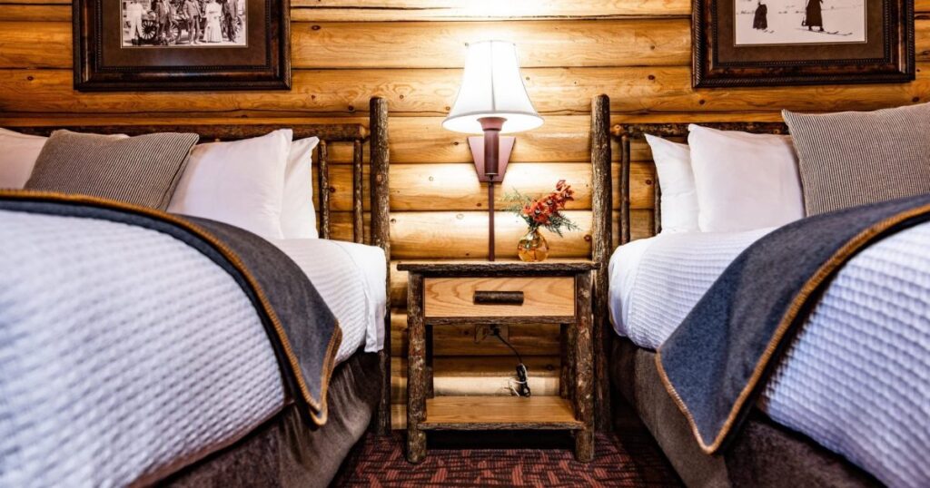 Inside a western themed log cabin guest bedroom with two beds and a lamp on