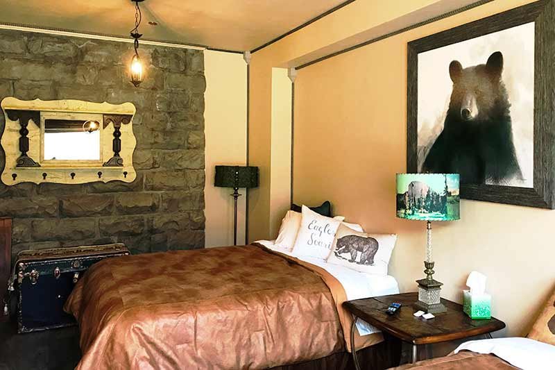 Inside a guest bedroom with photo of bear on the wall two beds with copper colored sheets and a feature wall