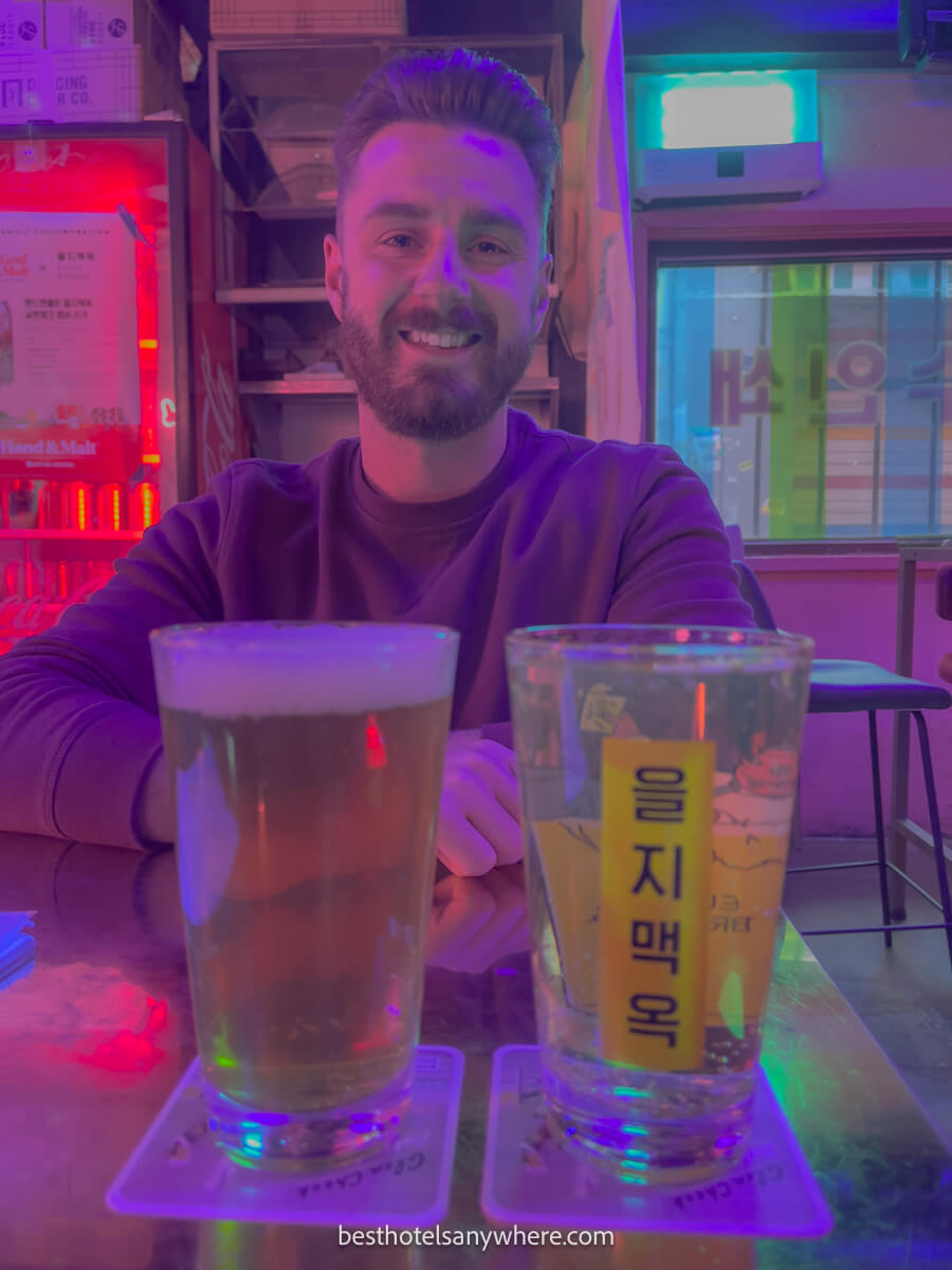 Tourist sat at a table with two beers and pink lights behind