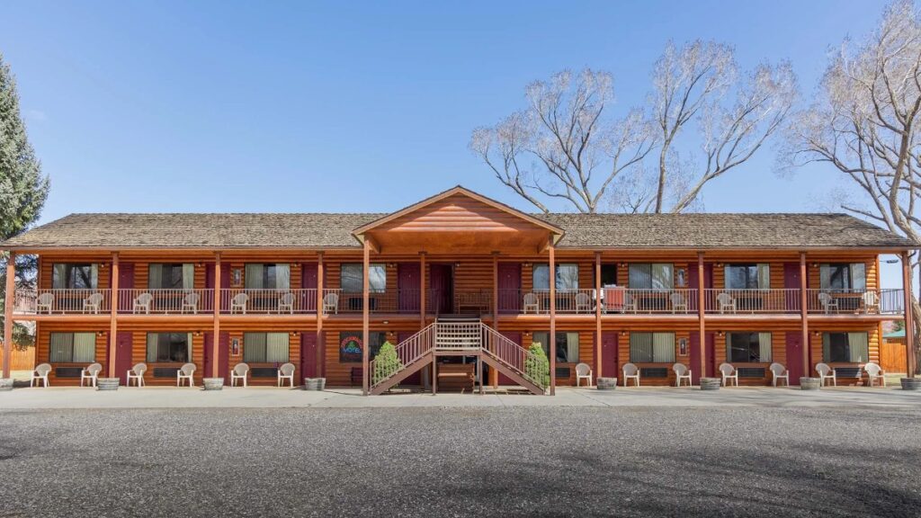 Exterior photo of a two story wooden motel with parking lot in front on a clear day
