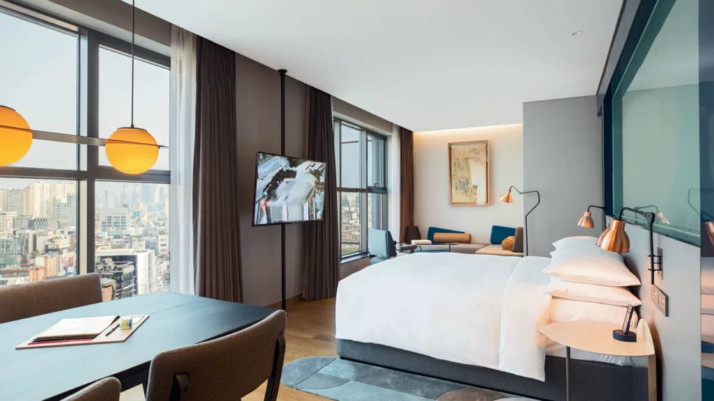 Inside an upscale hotel room in Seoul with bed desk and floor to ceiling windows