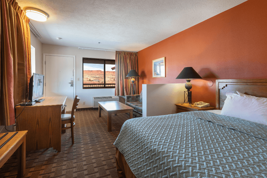 Inside a guest bedroom at a hotel in Torrey near Capitol Reef with bed sofa and desk leading to window with a view