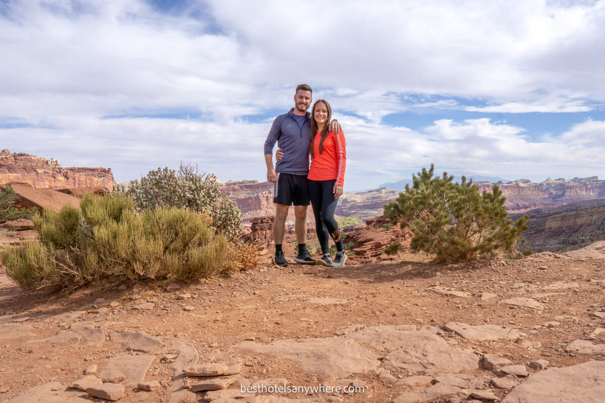 Couple standing on the edge of a red rock cliff with a canyon in the background on a cloudy day in Utah