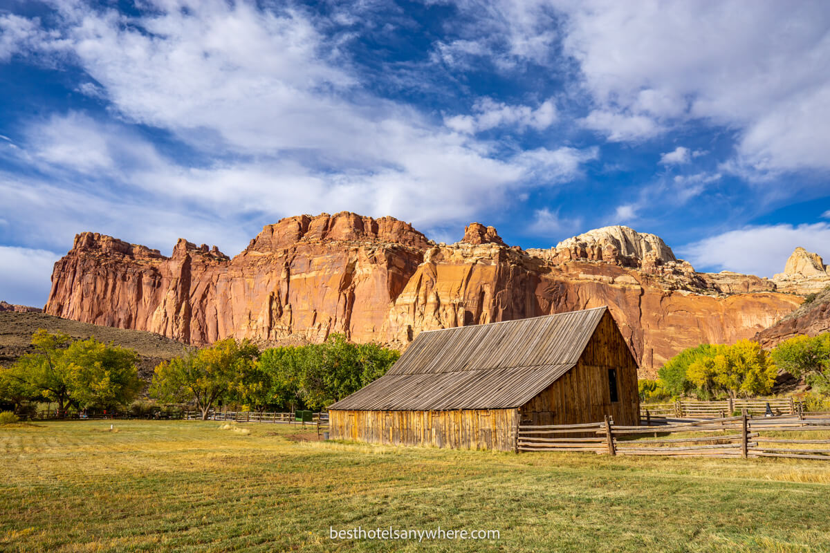 Fruita Barn on a meadow with tall red rock cliffs behind on a sunny day with blue sky