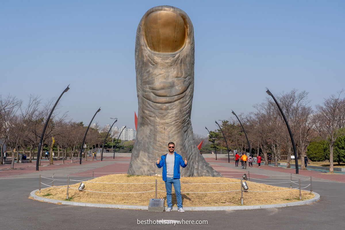 Tourist with thumbs up in front of a thumb statue in Seoul Olympic Park