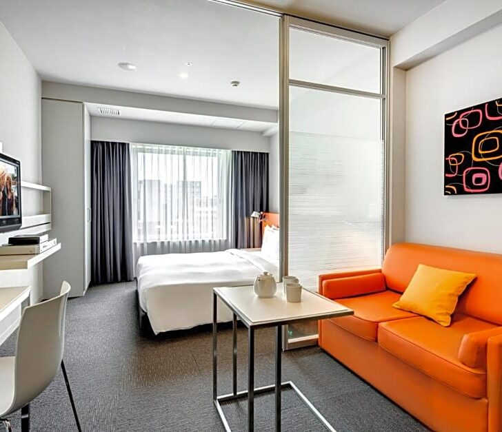 Inside an apartment style guest bedroom with orange sofa, table, bed and desk
