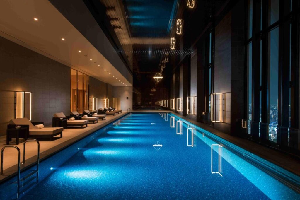 Long and narrow indoor swimming pool lit up at night with loungers to the side at Conrad Osaka
