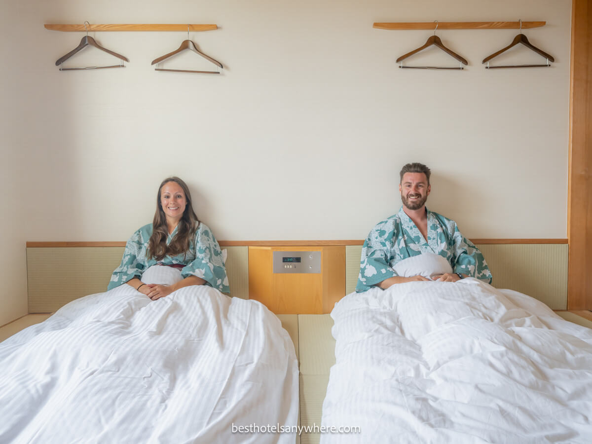 Mark and Kristen Morgan from Best Hotels Anywhere sitting up in twin beds on the tatami floor of the Hakone Lake Hotel in Japan wearing yukata