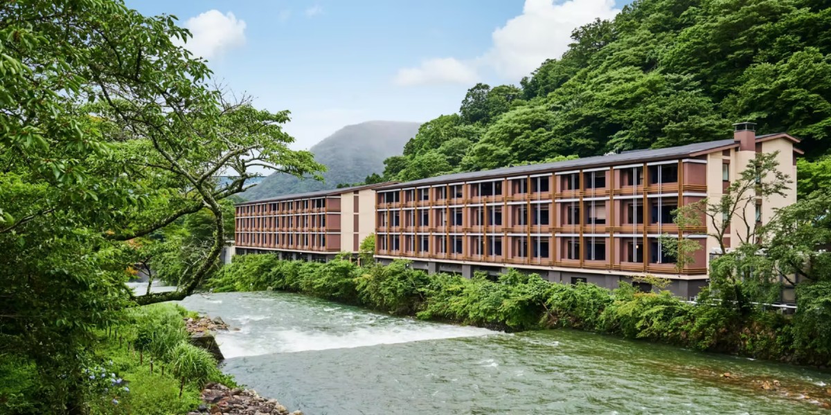 Long multi story building on the banks of a river with green vegetation behind