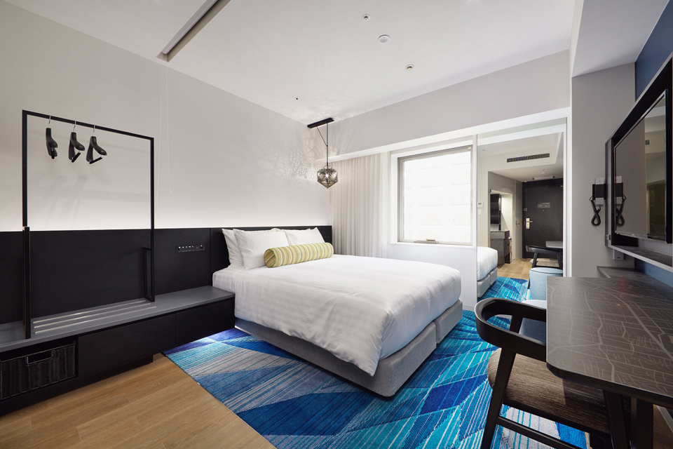 Inside a guest bedroom with large bed on blue rug leading to window