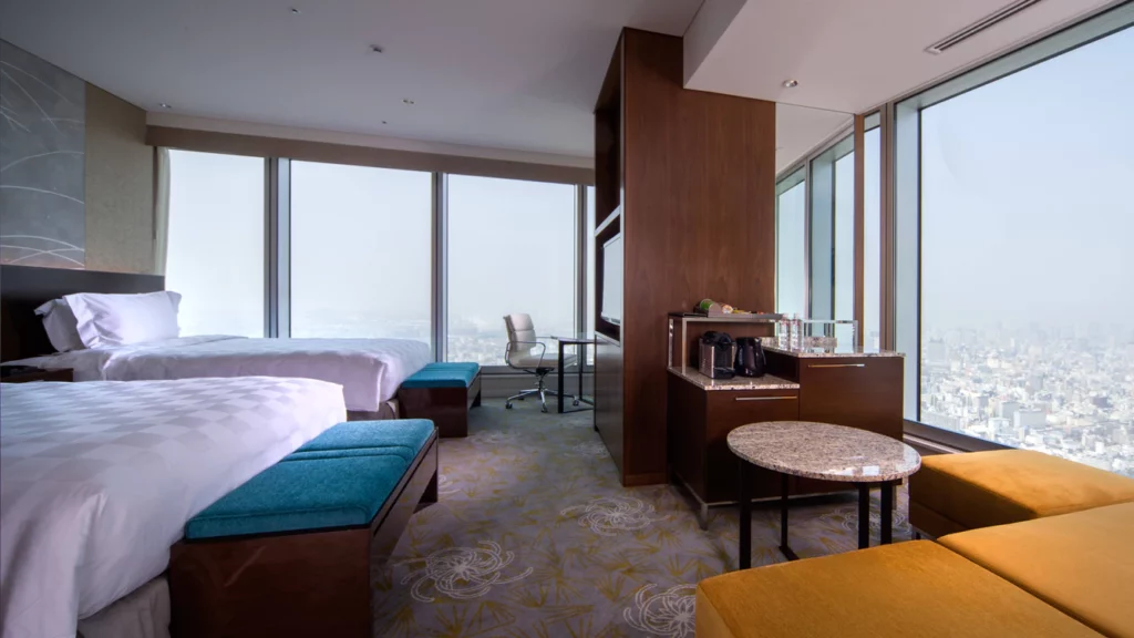Inside a guest bedroom with two beds and a desk leading to huge floor to ceiling windows