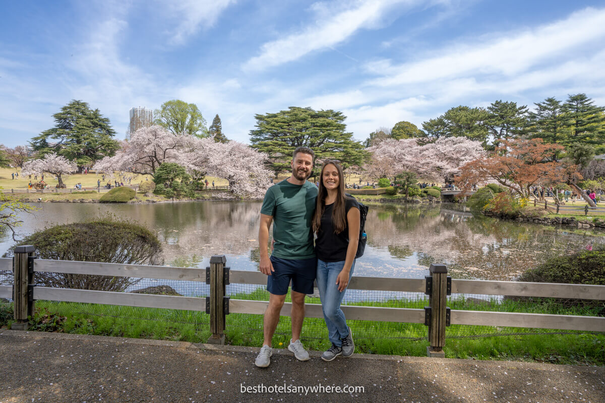 Couple standing together for a photo with Shinjuku Gardens in the background during cherry blossom season in Japan
