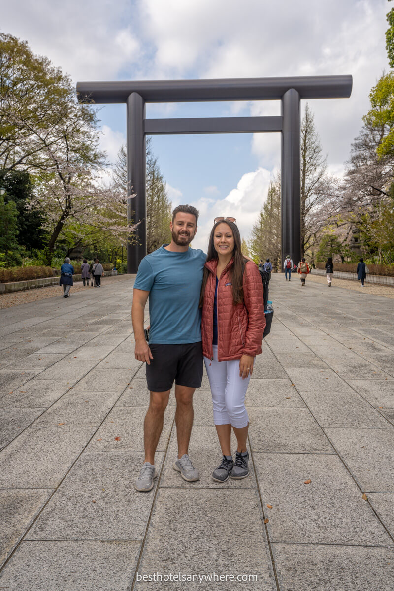 Photo of a couple standing below a tall torii gate in Tokyo