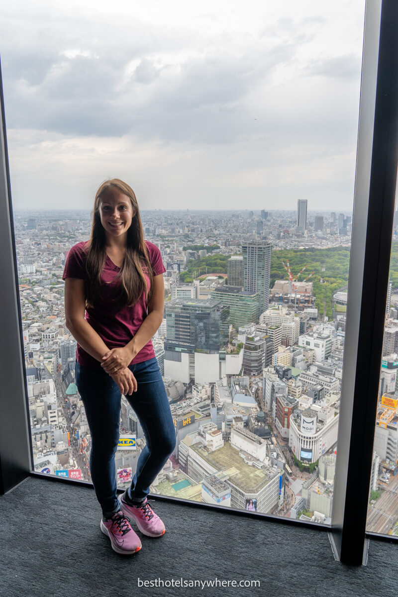 Tourist standing in front of a large floor to ceiling window in Shibuya Sky observation deck in Tokyo with a view over the city behind