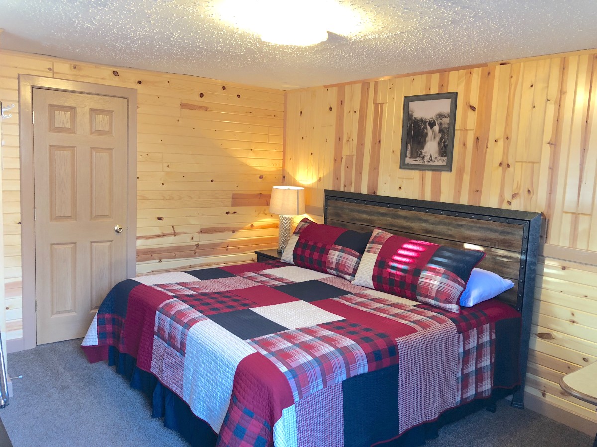 Inside a guest bedroom at a hotel in Keystone SD with wooden walls and a bed covered in a colorful blanket