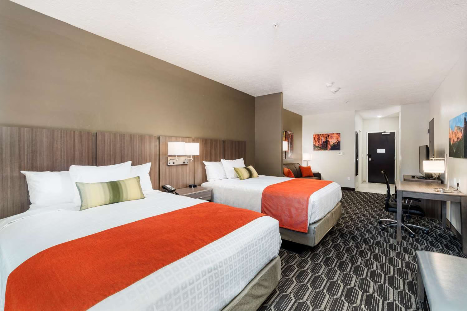 Two large beds with orange throws, desk with chair and sofa in a hotel in Springdale UT