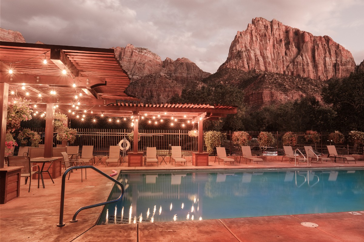 Photo of a swimming pool with sun loungers and distant towering red rocks in Zion
