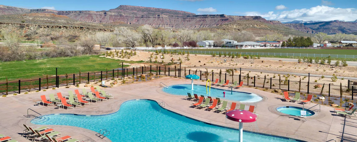 Photo of two swimming pools and a hot tub outdoors surrounded by grass and red rocks