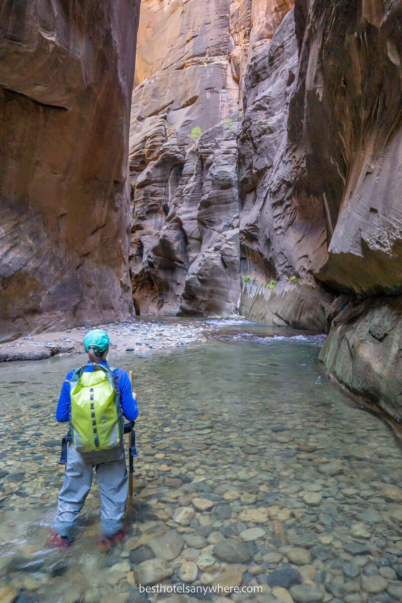 Hiker in waterproof clothing walking through The Narrows in Zion with a wooden pole