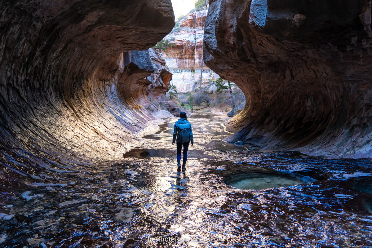 Hiker walking through The Subway in Zion with orange light illuminating the tunnel like formation