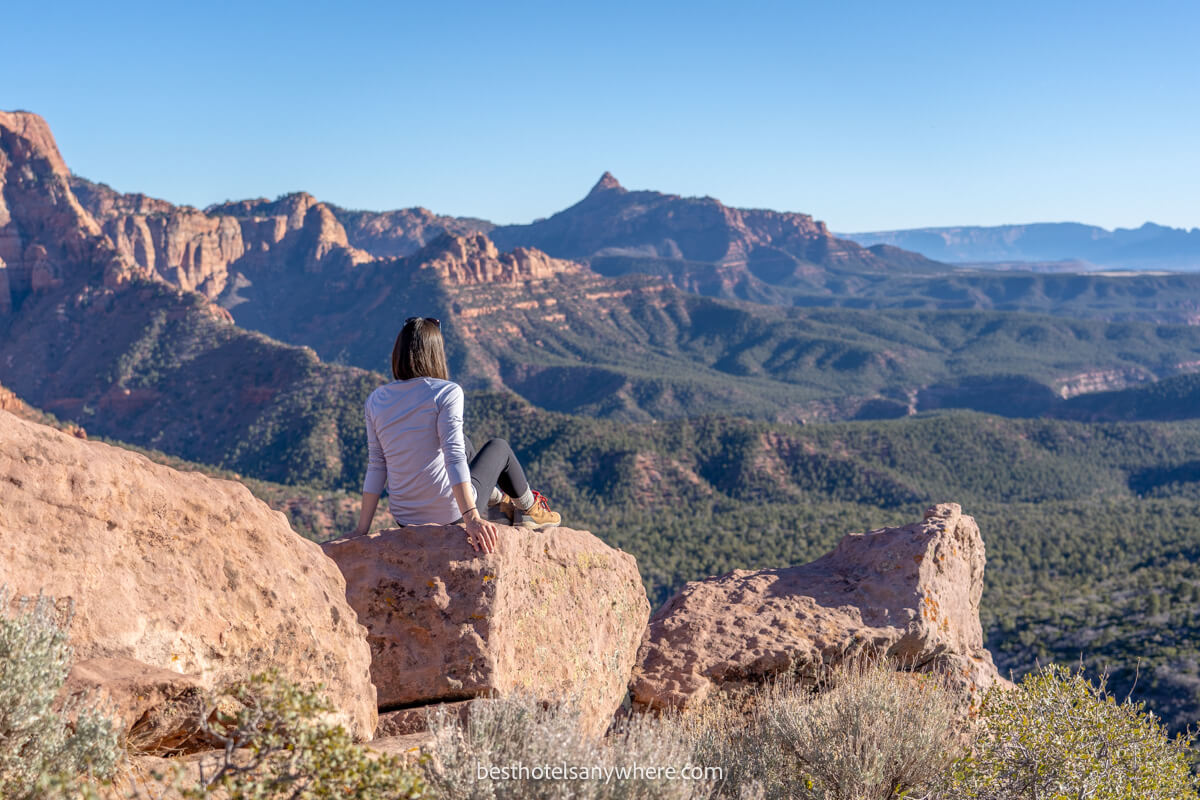 Hiker sat on a rock with arms back and far reaching views over a valley and red rock mountains