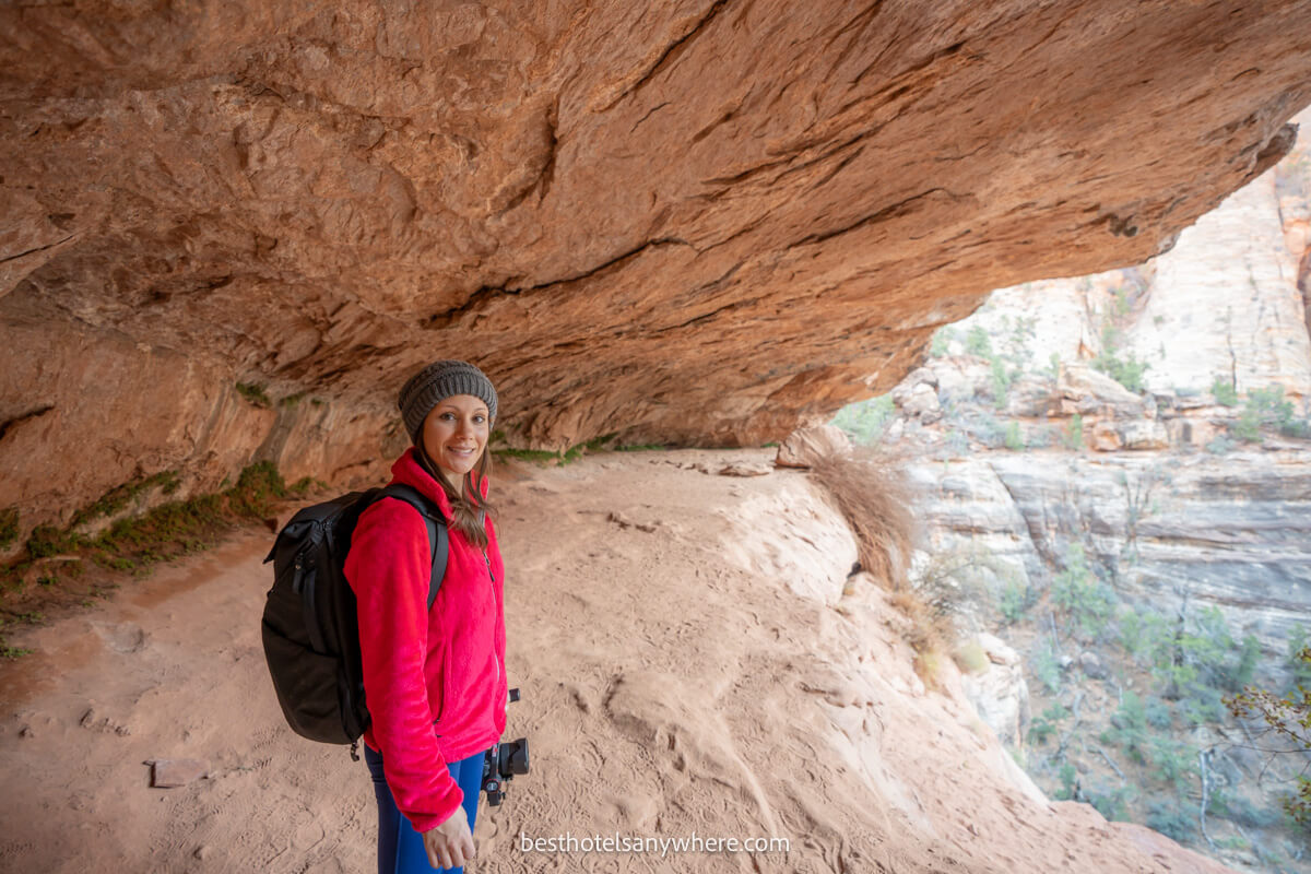 Hiker in pink fleece and backpack walking under an arching rock formation
