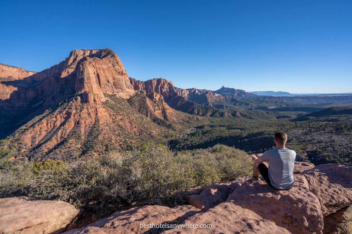 Hiker sat on a rock enjoying the view of distant red rock formations over a valley on a sunny day